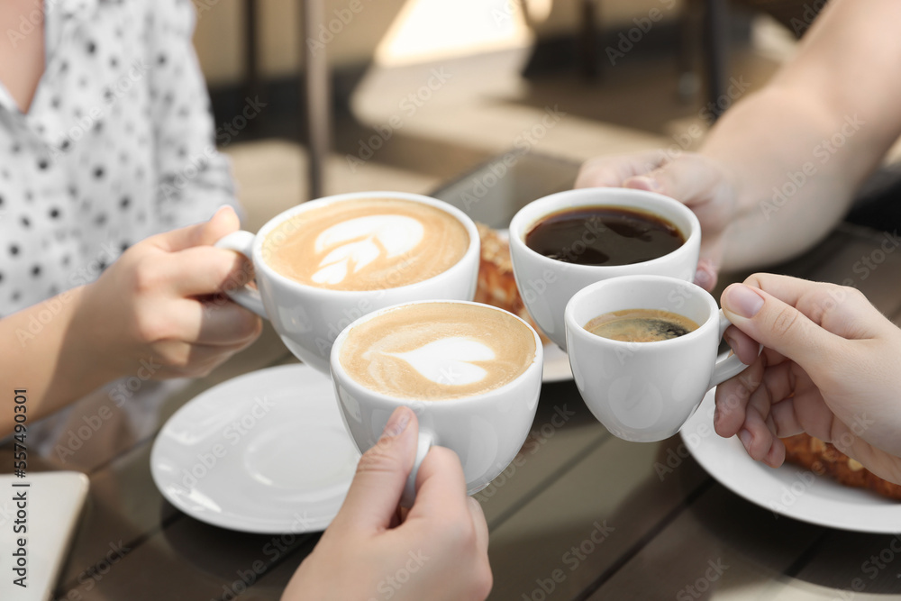 Friends drinking coffee at wooden table in outdoor cafe, closeup Friends drinking coffee at wooden table in outdoor cafe, closeup
