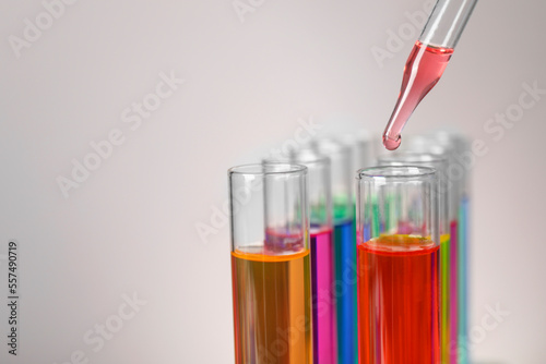 Dripping liquid from pipette into test tube on grey background, closeup. Space for text
