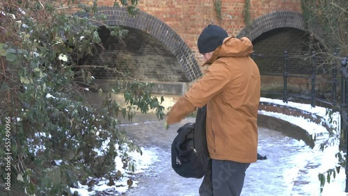 Warm dressed male putting drone carry bag into rucksack beside snow Brooklands lake archway photo