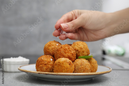 Woman salting fried tofu balls at light grey table, closeup