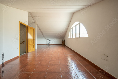 A large empty hall of a detached house in the attic with dormer windows of almost semicircular shape with oak door access to the stairs to change levels