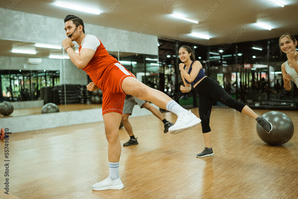 male instructor lifting legs sideways together with body combat training participants at the fitness center