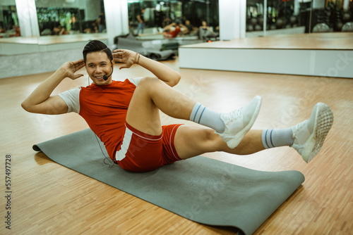 male instructor doing bicycle crunches on a mat in the gym photo