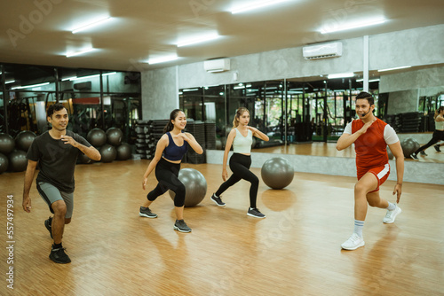 group of sporty men and women doing squats during exercise with instructor in fitness center