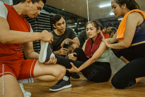 Asian woman with leg cramps is helped by her friends and instructor during exercise