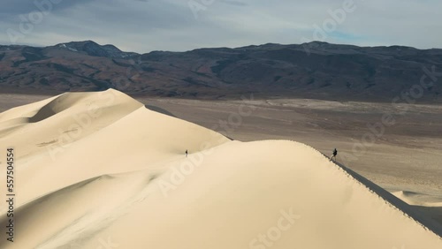 A male hiker walks across the ridge line of the Eureka Dunes at sunrise in Death Valley National Park in California. The Eureka Valley and Saline Mountain ranges are seen in the background.