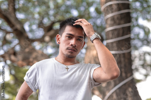 A moreno Filipino model wearing a white shirt poses with a fierce look on his face while fixing his hair in the middle of the day at the garden.