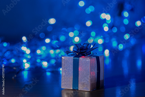 Gift box tied with a ribbon on a blue background of a glowing garland. © Andrey Nikitin
