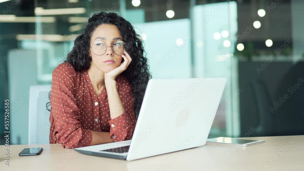 bored woman at the workplace. Young Hispanic female employee in the office is sad sitting at a laptop computer worker sitting at desk feeling sleepy does not want to do work project bored woman at the workplace. Young Hispanic female employee in the office is sad sitting at a laptop computer worker sitting at desk feeling sleepy does not want to do work project
