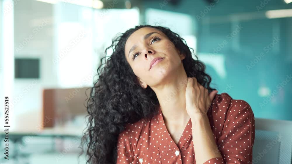 young curly brunette woman having neck pain while sitting in office at workplace. Female massages shoulder muscles. pain and discomfort from prolonged work. office syndrome young curly brunette woman having neck pain while sitting in office at workplace. Female massages shoulder muscles. pain and discomfort from prolonged work. office syndrome