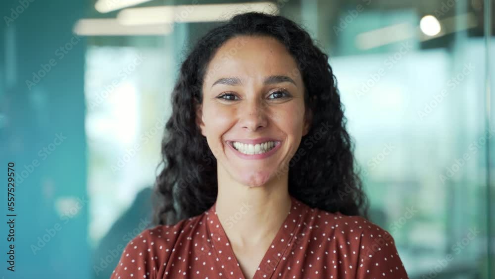 Portrait of happy beautiful hispanic young woman creative employee looking at camera and smiling in modern office. Curly brunette in casual business woman worker indoors