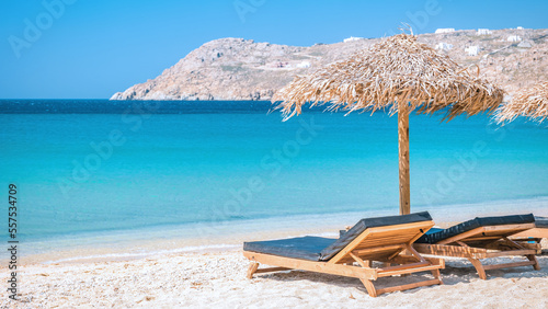 Fototapeta Naklejka Na Ścianę i Meble -  Mykonos beach during summer with umbrella and luxury beach chairs beds, blue ocean with a mountain at Elia beach Mikonos Greece beach