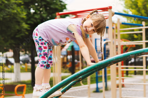 A cheerful, charming little girl climbed the iron stairs to the playground on a sunny day. A happy, smiling four-year-old girl climbs the stairs. Games for the development of children in the fresh air