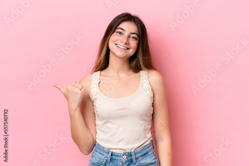 Young caucasian woman isolated on pink background pointing to the side to present a product