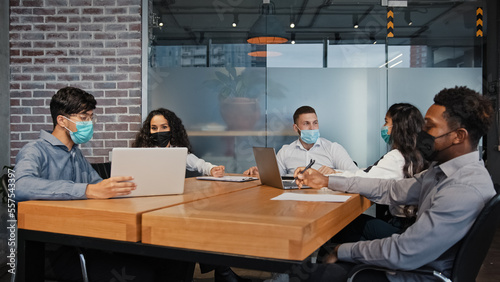 Diverse business team people workers in medical masks working together in office multiracial colleagues multiethnic group teamwork discussing project work in conference room check papers online data