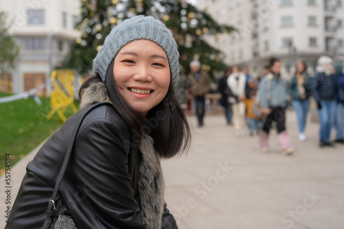 outdoors urban portrait of young happy and beautiful Asian Chinese woman in leather coat and beanie taking a walk relaxed in city business district smiling cheerful