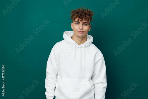 a cute, funny, joyful man stands on a green background in a white hoodie and looks pleasantly into the camera. Horizontal studio photo for inserting an advertising layout