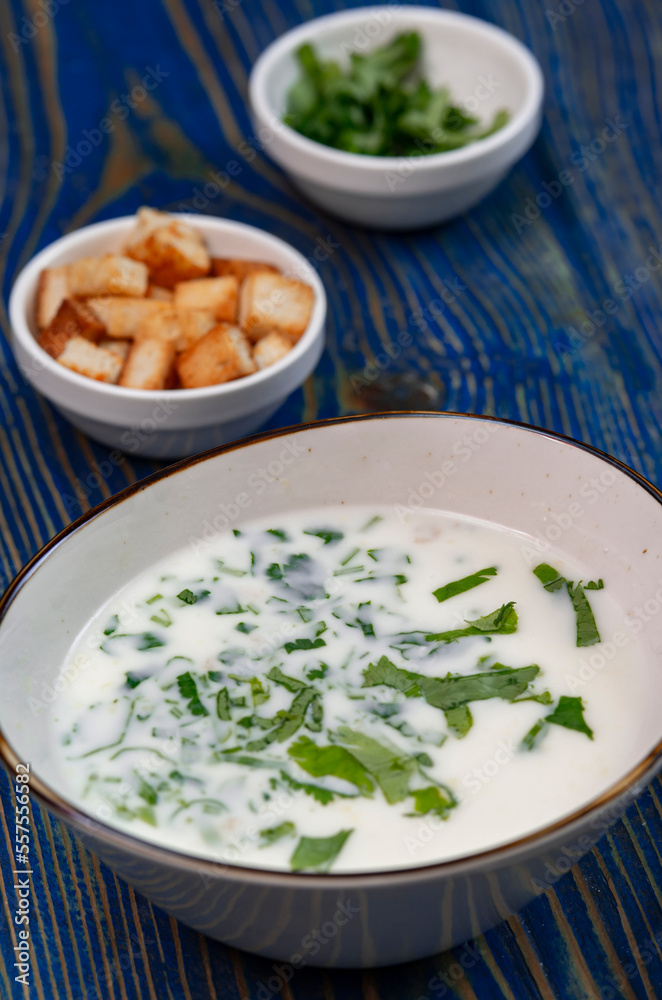 yogurt soup with herbs and crackers on a blue wooden table