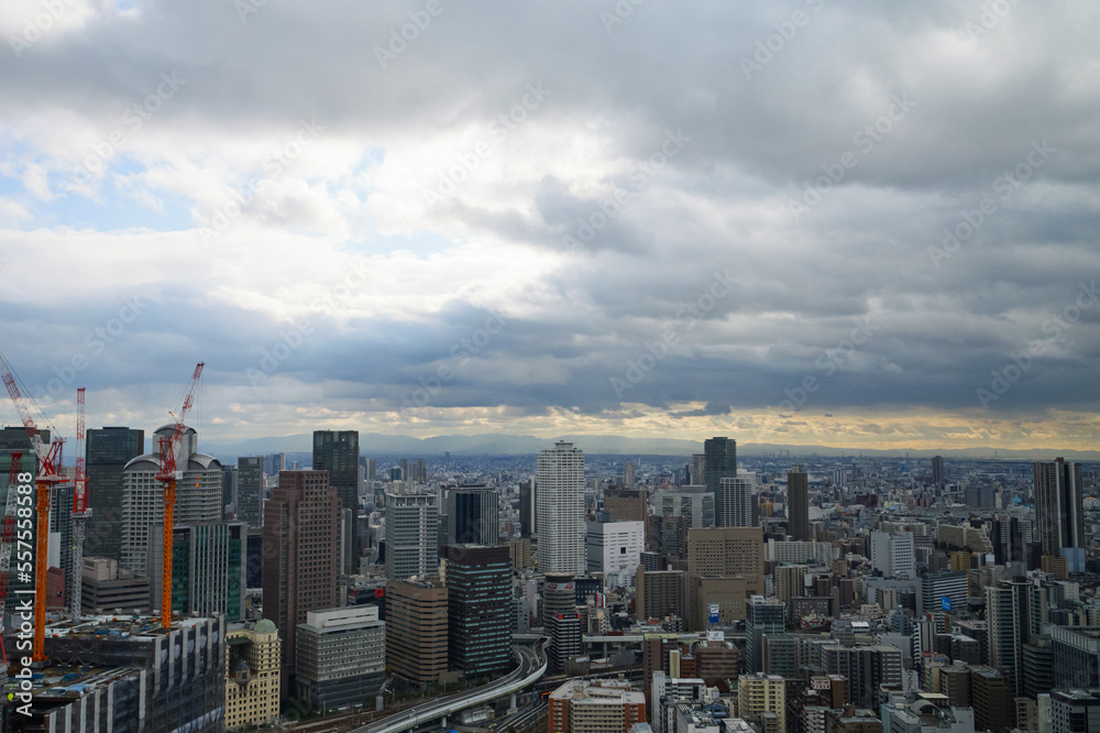 Fototapeta premium Overhead view of Osaka's Umeda area from a hill on a cloudy day, sunlight shining through a gap in the clouds.