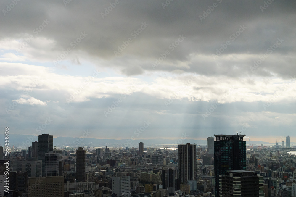 Overhead view of Osaka's Umeda area from a hill on a cloudy day, sunlight shining through a gap in the clouds.