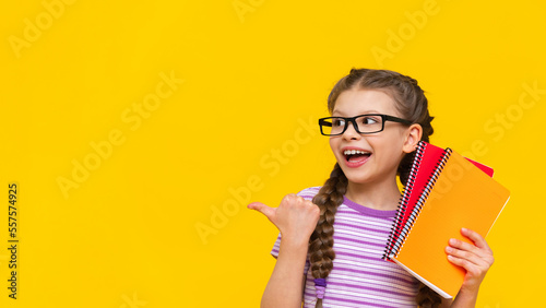 The little girl points her finger to the side and smiles. A schoolgirl with pigtails and glasses on an isolated background.