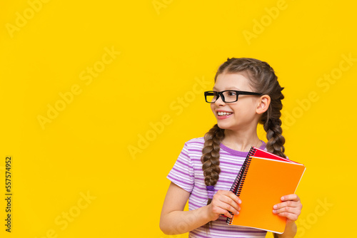 The girl is holding a book and looking away. Cute little girl on yellow isolated background.