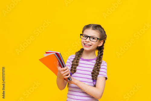 The girl shows her notebooks and rejoices. a child on a yellow background. A little girl with glasses.
