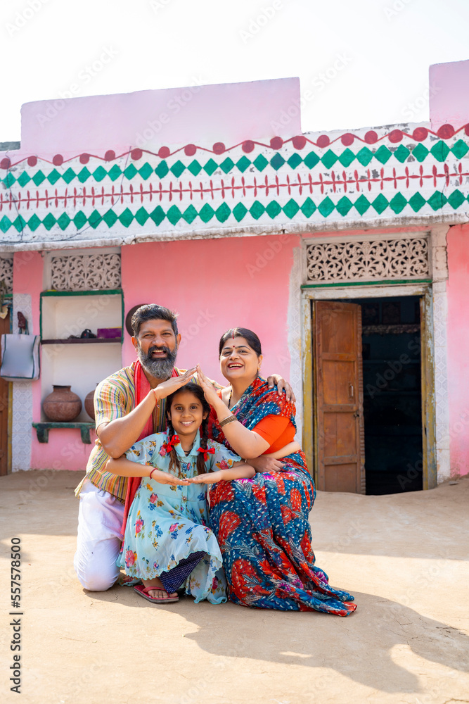 Fototapeta premium Happy Indian farmer with wife and daughter making home shape with hand. dream home concept.