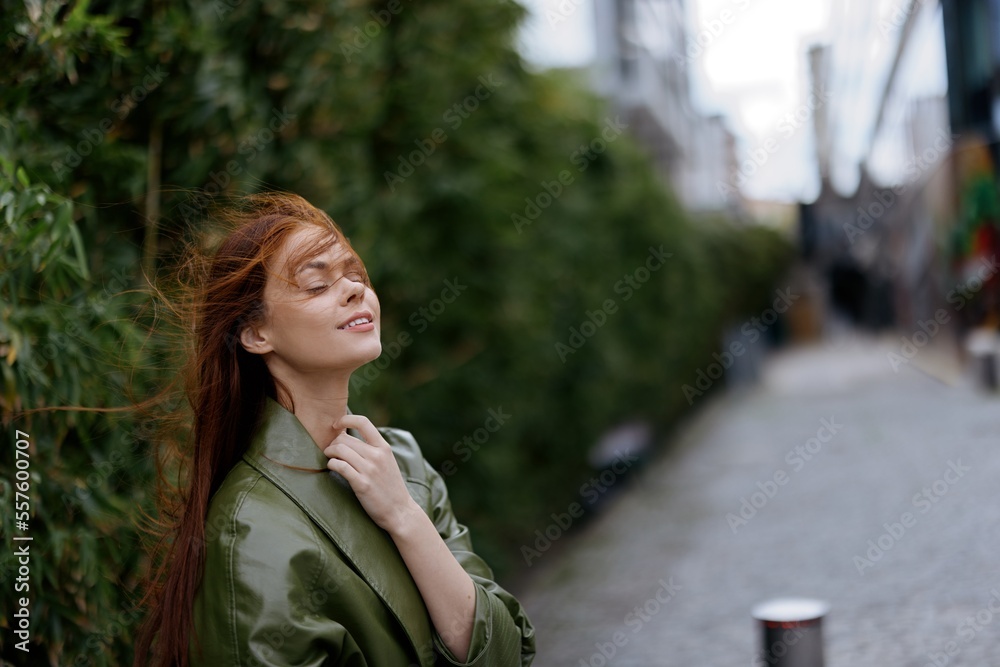 Naklejka premium Woman with a beautiful smile posing against a green bamboo in spring, red flying hair in the windy weather, the concept of style and fashion in the city