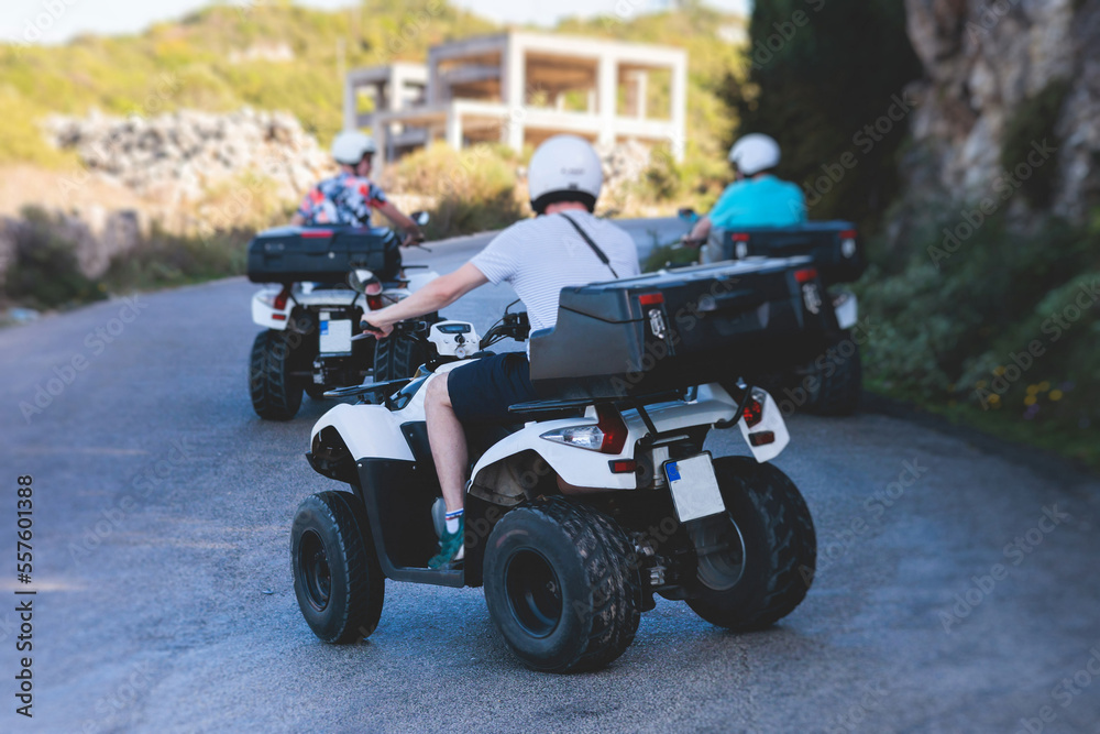 Obraz premium Group of riders riding ATV vehicle crossing mountain serpentine road track, process of driving rental vehicle, all terrain quad bike vehicle, during off-road tour, Greece, Ionian sea islands