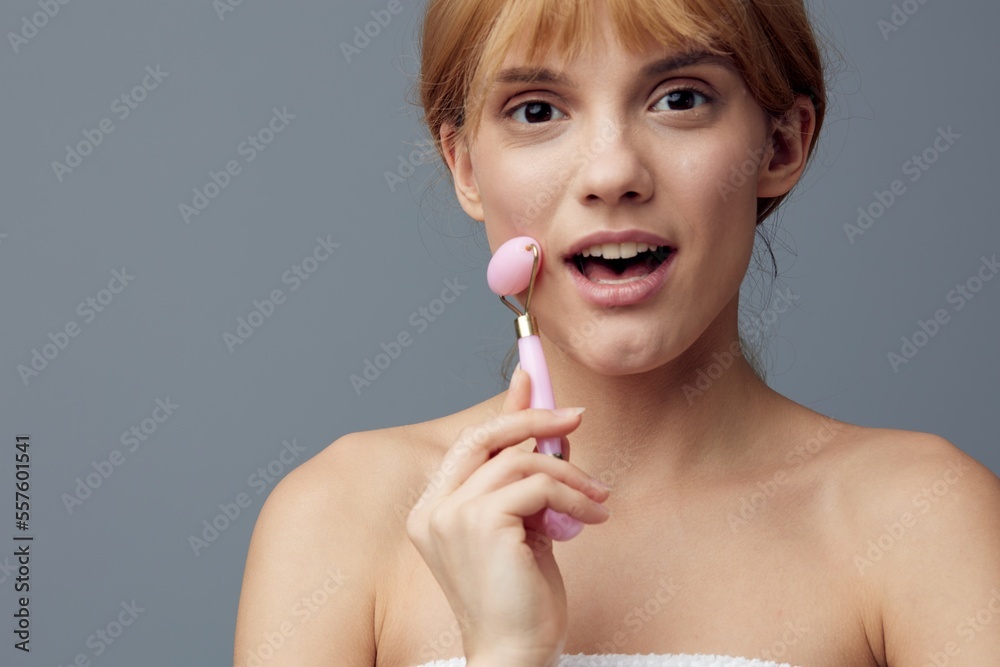 custom made wallpaper toronto digitala joyful, delighted woman with perfect skin stands on a gray background and does a facial massage with a pink roller, smiling pleasantly. Close horizontal photo with empty space