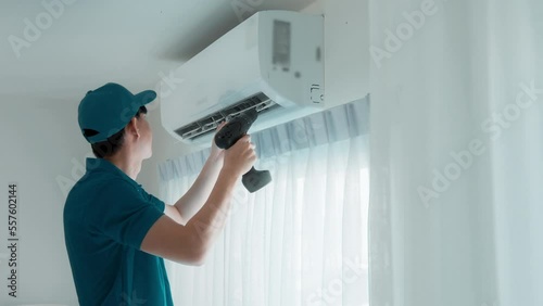 An Asian young Technician service man wearing blue uniform checking ,  cleaning air conditioner in home