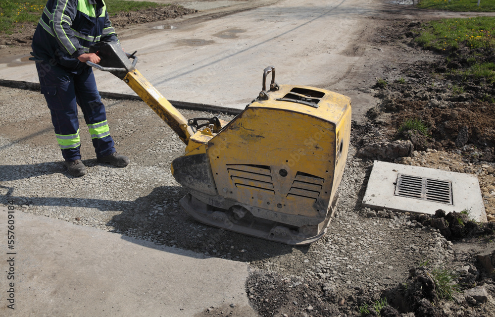 Worker use vibratory plate compactor compacting gravel at road