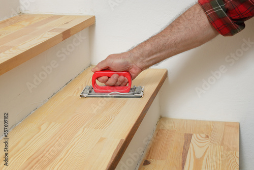 Closeup of worker hand sanding wooden stairs using  hand tool