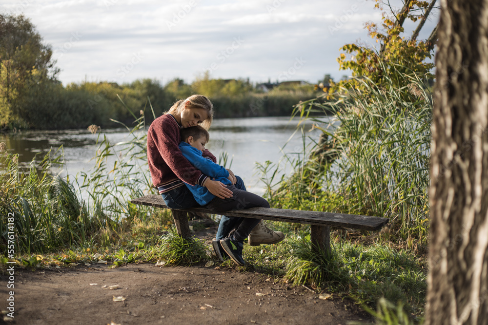 Mother hugging boy outdoors on the bench. Mother kissing son in the park. Precious moments between mom and son Mother hugging boy outdoors on the bench. Mother kissing son in the park. Precious moments between mom and son