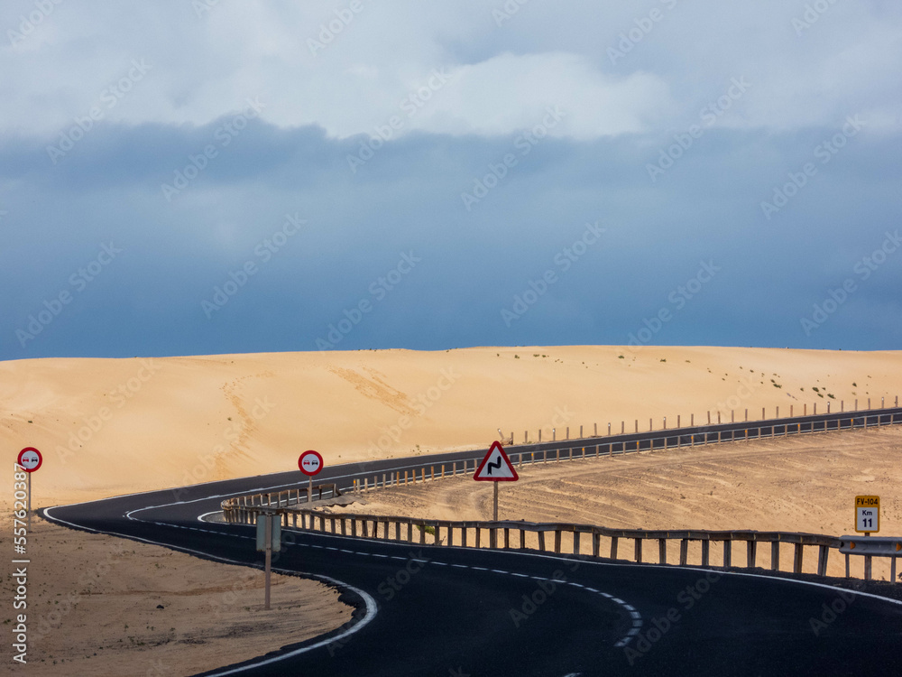 Winding road between dunes with cloudy sky