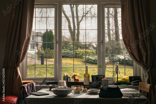 A living room with a table in front of a window overlooking a sunlit lawn. On the table are various household items. Scotland, United Kingdom