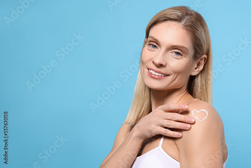 Woman with body cream onto her arm against light blue background, space for text