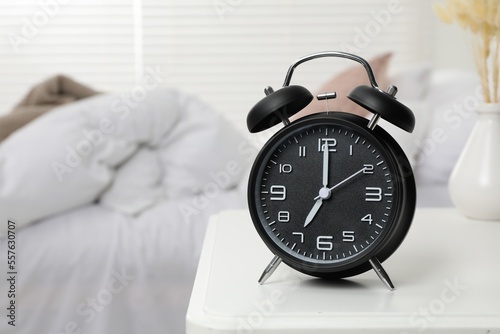 Black alarm clock on white wooden nightstand in bedroom, space for text