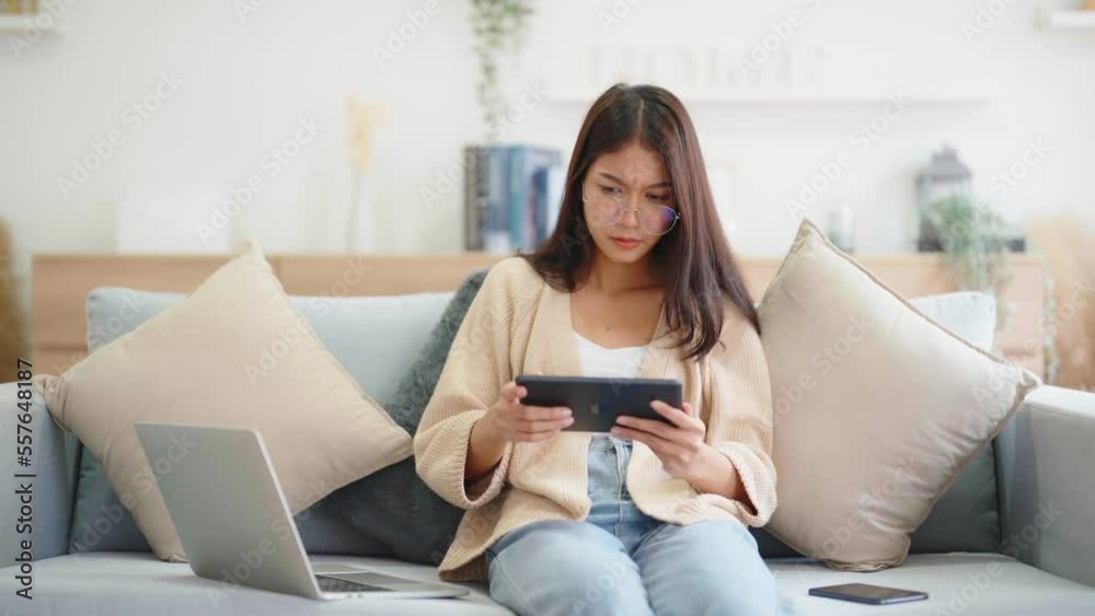 Young asian woman using computer laptop, tablet and mobile smartphone while seated on couch at home Young asian woman using computer laptop, tablet and mobile smartphone while seated on couch at home