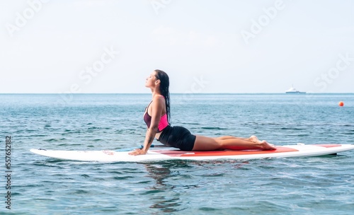 Woman sup yoga. Happy young sporty woman practising yoga pilates on paddle sup surfboard. Female stretching doing workout on sea water. Modern individual female outdoor summer sport activity. © panophotograph