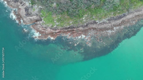 Drone video flying over the coastline of Shark Island, Fingal Bay with beautiful blue water and waves crashing on rocks
