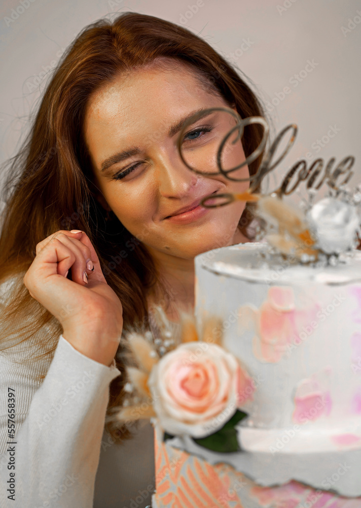 A beautiful girl confectioner shows a cooked two-tiered wedding cake decorated with fresh flowers. A beautiful girl confectioner shows a cooked two-tiered wedding cake decorated with fresh flowers.