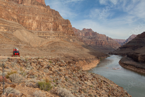 Landscape view from within Grand Canyon, Arizona, with mountain rock cliffs, meandering river and blue sky with clouds, red helicopter parked on ridge, outdoor daylight.
