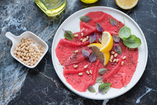 White plate with carpaccio beef, lemon and pine nuts on a black marble background, horizontal shot, high angle view