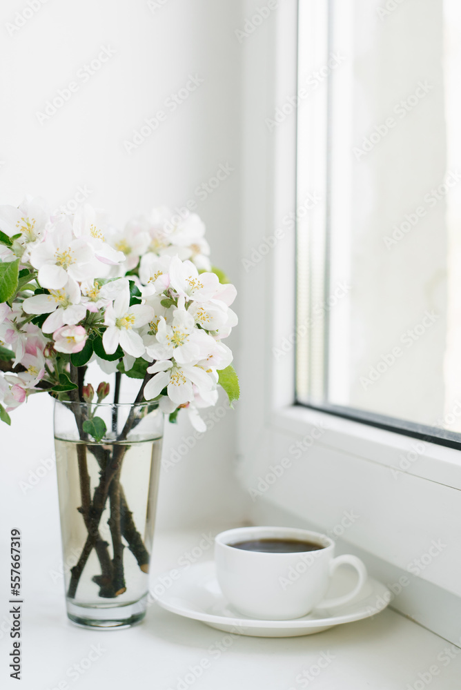 Spring flowers in a vase and a cup of tea or coffee in a white porcelain mug on the windowsill