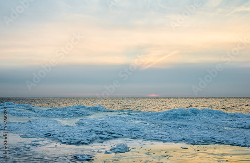 Blue frozen ice layer on beach side next to sea