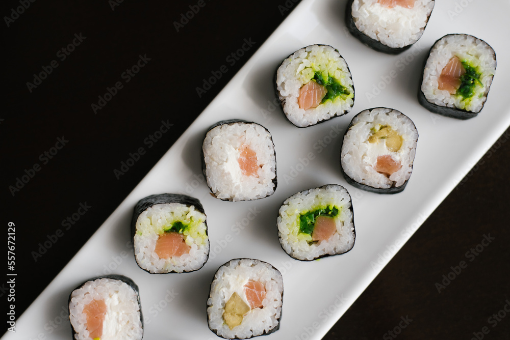 Rolls with cheese and salmon on a white rectangular plate on a dark background. Rolls with cheese and salmon on a white rectangular plate on a dark background.
