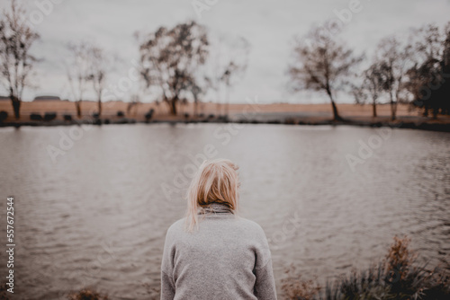 Blonde woman isolated sitting on a bench in front of lake © Kaspars