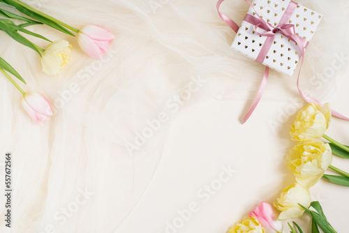 Flower arrangement and gift box with a bow for your birthday. Pink and yellow flowers on a beige background.valentine's day. Flat lay, top view, copy space